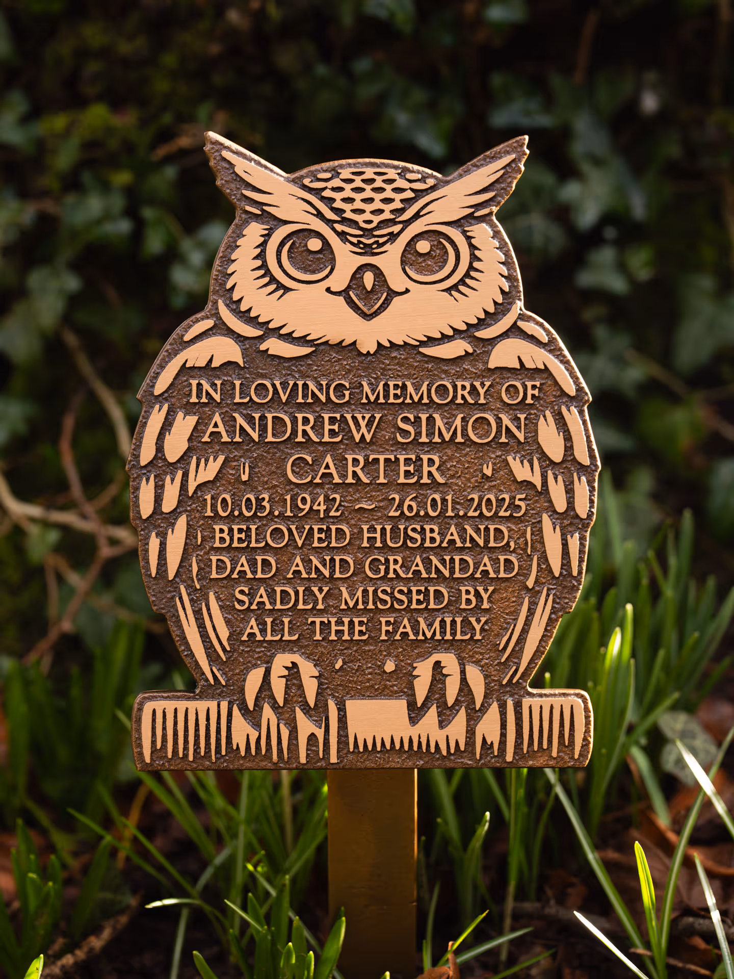 Angled view of a cast bronze owl memorial plaque with raised text on a ground stake.