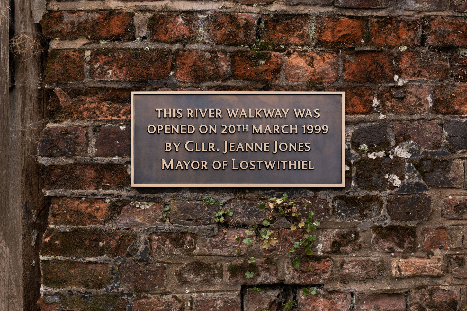 Cast bronze commemorative plaque on a brick wall marking the opening of the Lostwithiel river walkway on 20 March 1999 by Mayor Jeanne Jones.