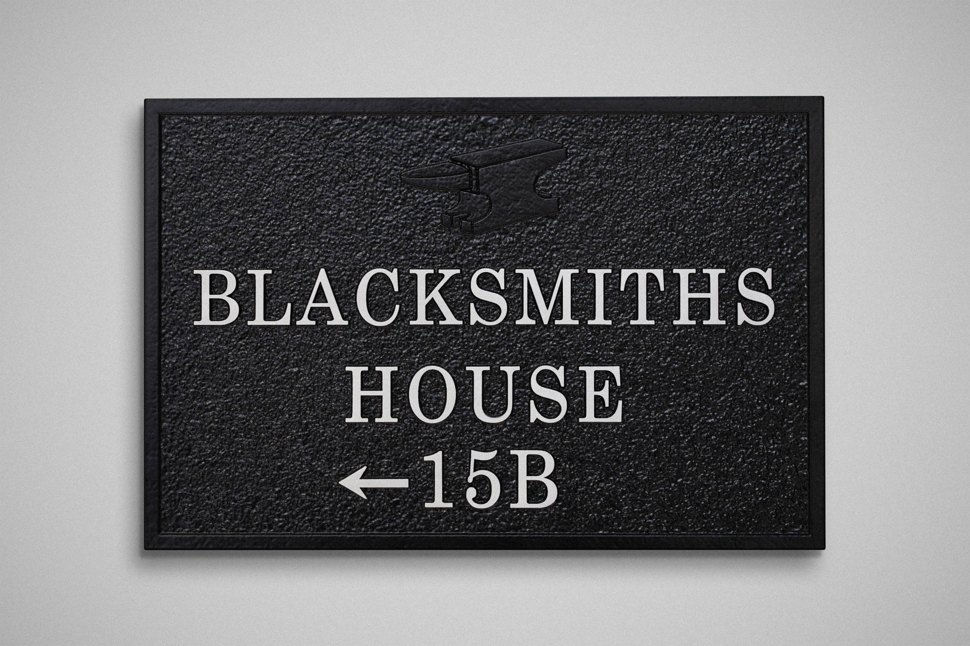 Bespoke cast aluminium house sign reading 'Blacksmiths House 15B' with raised anvil motif, powder-coated black, mounted on a white wall – handcrafted by Anglia Sign Casting.