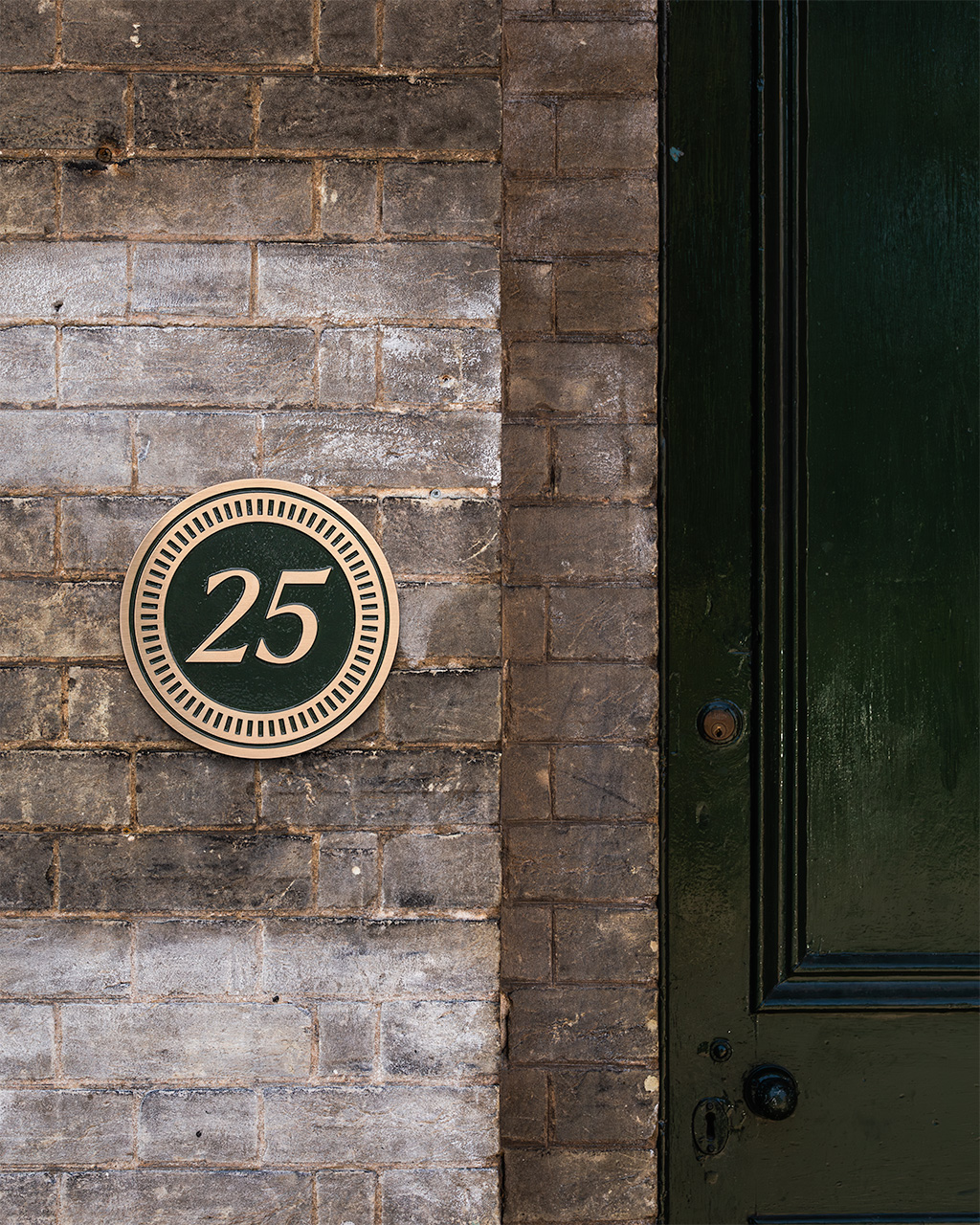 A custom luxury house sign featuring a circular bronze plaque with a painted deep green background and gold lettering. The sign displays the house number 25 in elegant raised lettering, framed in a decorative border. Crafted with precision, this bespoke house plaque combines timeless style with premium quality, making it an ideal choice for personalised home signage or custom bronze house number signs.