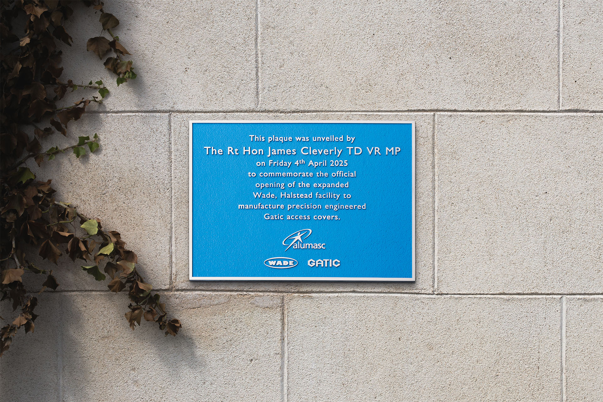 A cast aluminium commemorative plaque, crafted for Wade, Halstead. The plaque features raised lettering on a textured blue background with a silver border. It marks the official opening of the expanded Wade facility for manufacturing precision-engineered Gatic access covers, unveiled by The Rt Hon James Cleverly TD VR MP on 4th April 2025. The design includes the Alumasc, Wade, and Gatic logos at the bottom. Made to celebrate a milestone in the company's growth and innovation.