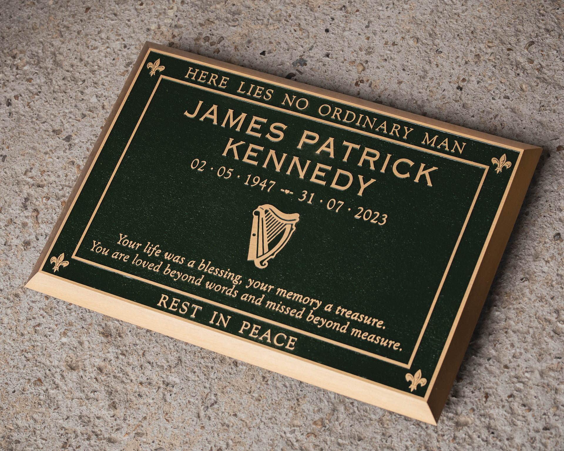 Large cast bronze memorial lawn tablet with a green painted background, commemorating the life of James Patrick Kennedy. Featuring gold lettering, decorative fleur-de-lis corner details, and an engraved Irish harp motif. A timeless Irish memorial plaque, crafted to honour a loved one with dignity and remembrance.