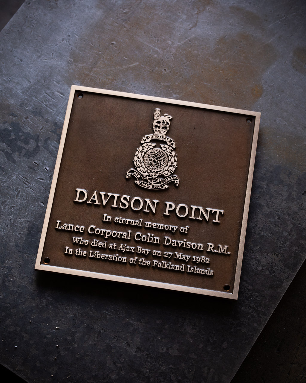 A square bronze military memorial plaque, dedicated to Lance Corporal Colin Davison R.M., who died at Ajax Bay on 27 May 1982 during the liberation of the Falkland Islands. The plaque is titled Davison Point and features the emblem of the Royal Marines at the top, with raised bronze lettering set against a textured background. Crafted with care, the plaque serves as a lasting tribute to a fallen hero.