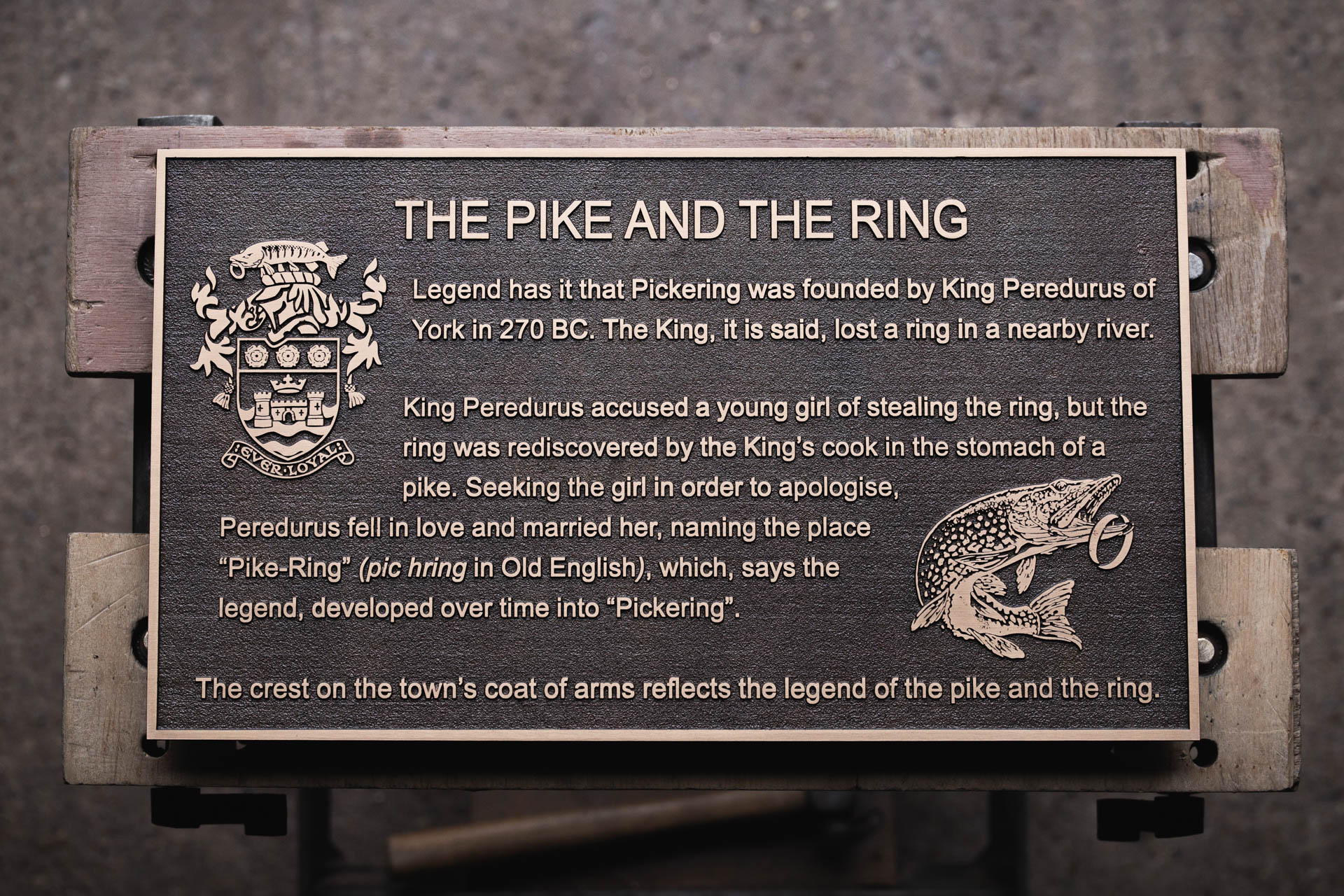 A cast bronze historical plaque titled The Pike and the Ring, crafted for Pickering Town Council. The plaque features raised lettering and a detailed pike motif, illustrating the local legend of how Pickering got its name. The town's crest is displayed on the left, with a patinated background contrasting against polished bronze highlights. Made by Anglia Sign Casting to commemorate Pickering’s heritage.