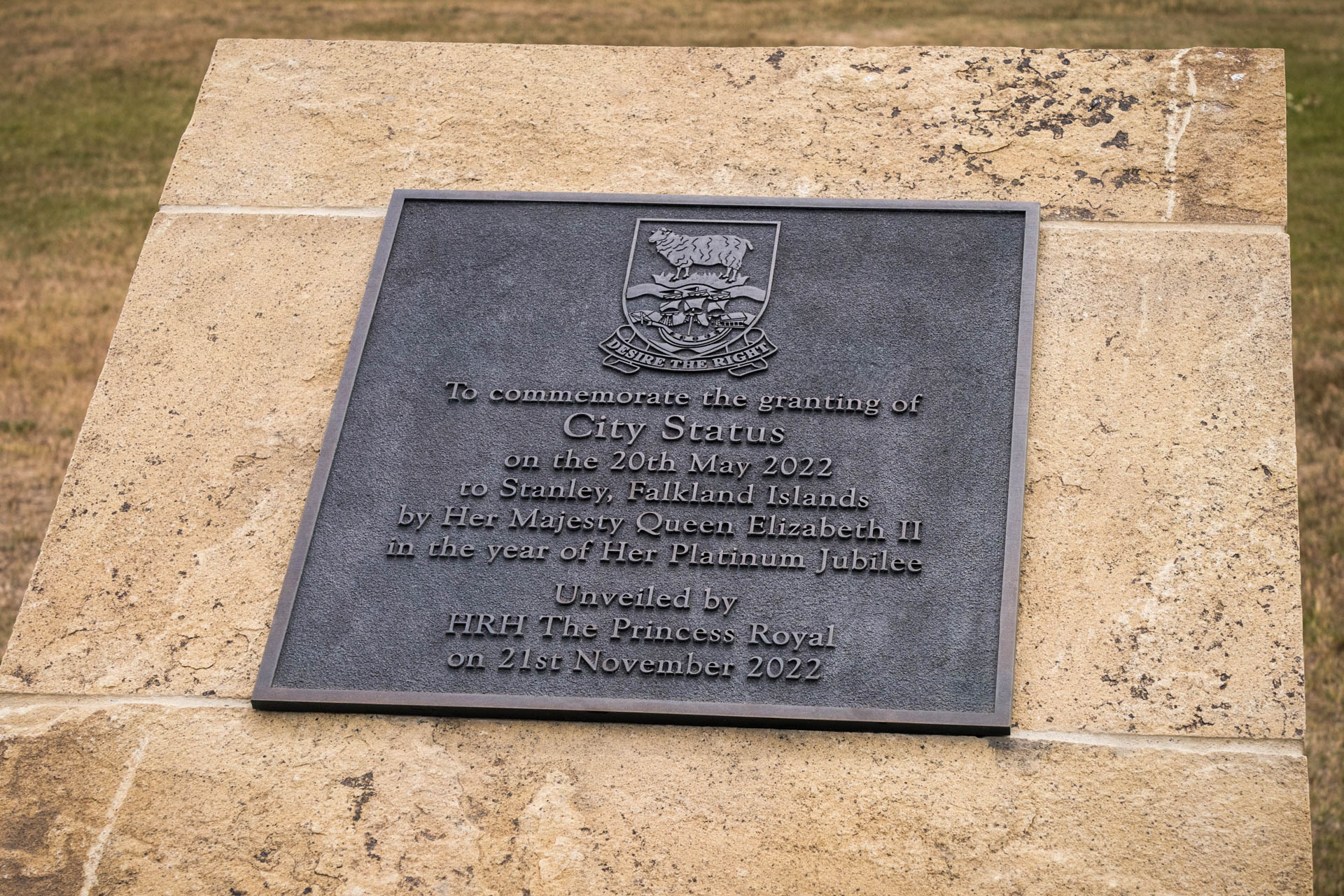 A cast bronze commemorative plaque marking the granting of city status to Stanley in the Falkland Islands. Featuring raised lettering with a patinated finish, the plaque displays the Falkland Islands' coat of arms at the top and is mounted on a stone plinth. Made from durable bronze by Anglia Sign Casting to honour the occasion in 2022.