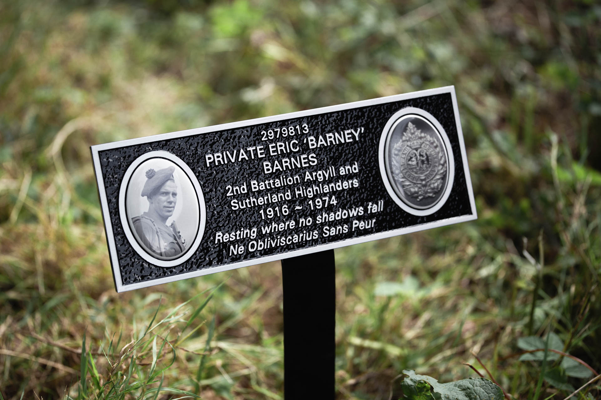 Cast aluminium memorial plaque on a stake, dedicated to Private Eric Barnes of the Argyll and Sutherland Highlanders. Finished in black with silver lettering and two raised cameos — one featuring a portrait of Private Barnes and the other displaying the regiment's emblem. A timeless tribute designed to stand the test of time outdoors.