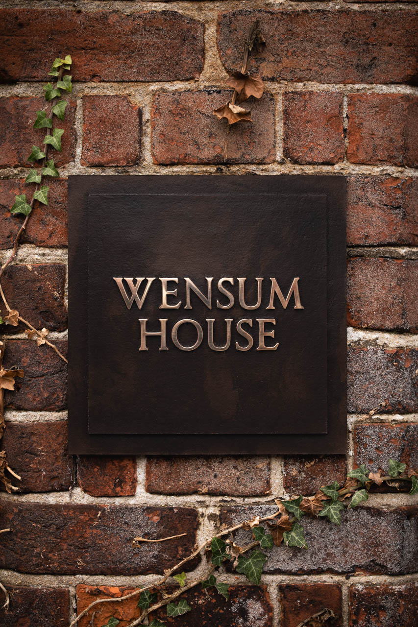 A handcrafted cast bronze house sign for Wensum House, featuring raised bronze lettering on a textured dark bronze background, exuding timeless elegance and quality craftsmanship.