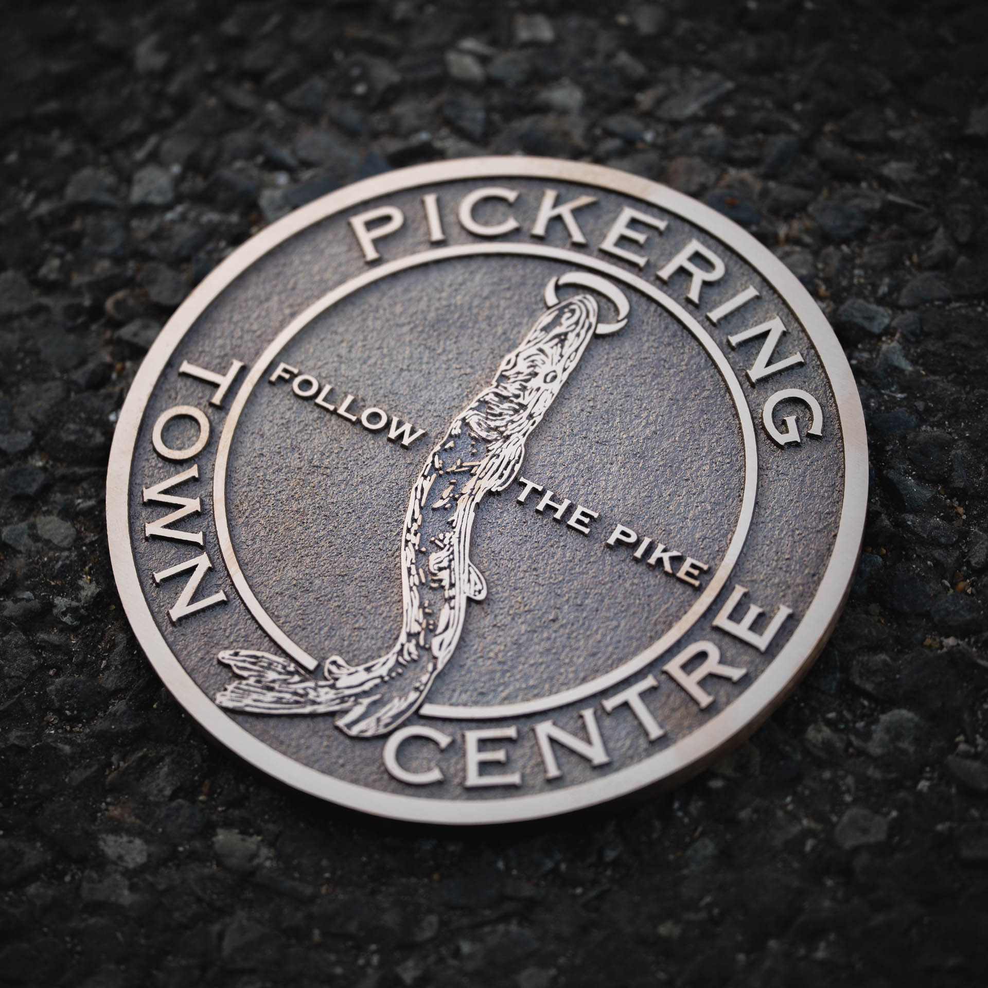 Durable cast bronze metal floor marker for Pickering Town Council, crafted using traditional casting techniques for a timeless finish. Featuring raised lettering with the phrase 'Follow the Pike' and an intricate pike fish design — guiding visitors through the town centre. Made from long-lasting, weather-resistant materials with sustainability in mind.