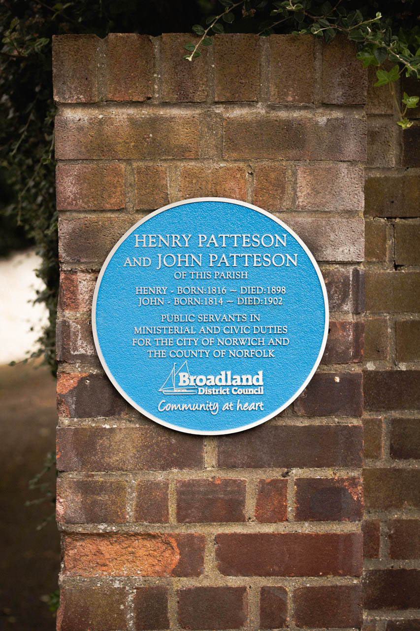 Circular blue heritage plaque commemorating Henry Patteson and John Patteson, public servants in ministerial and civic duties for Norwich and Norfolk. Affixed to a brick wall, this cast aluminium plaque features raised silver lettering and is commissioned by Broadland District Council as part of a historical recognition initiative. Designed for durability, ideal for marking historical sites and notable figures.
