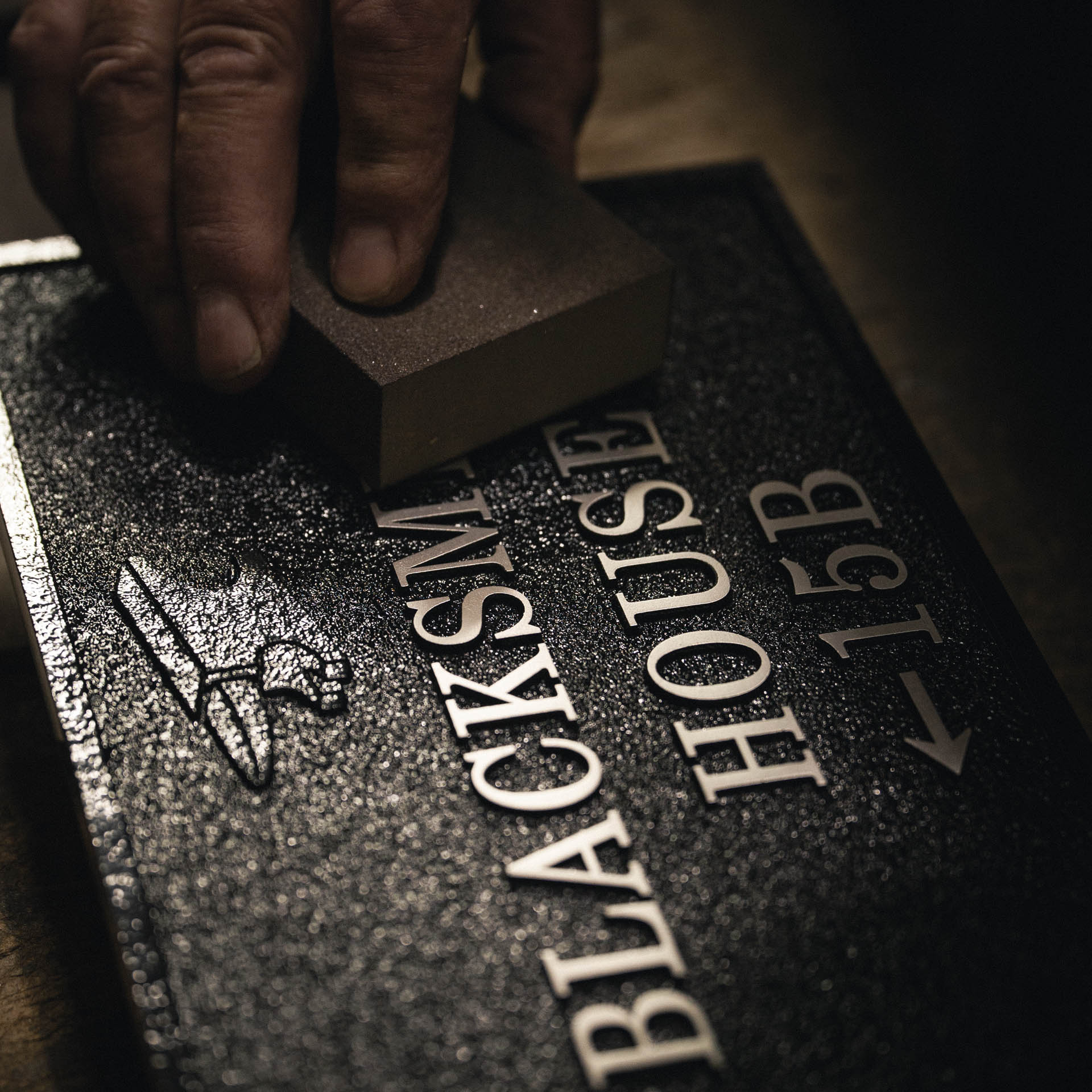 Craftsman linishing raised lettering on bespoke aluminium house sign to reveal polished silver finish.