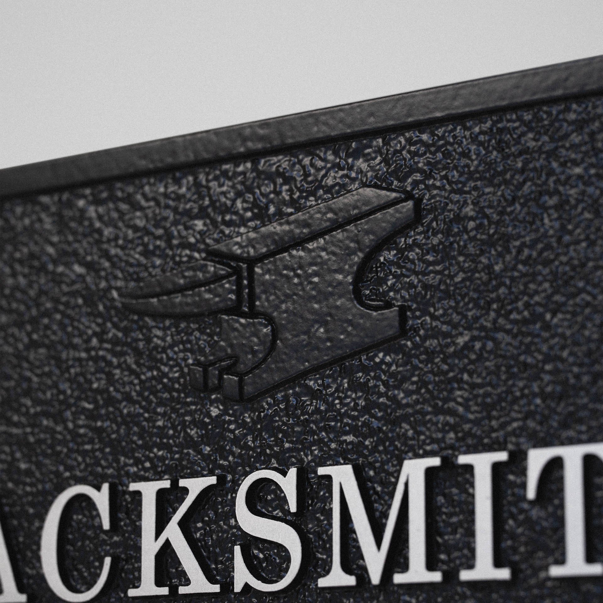 Detail of anvil motif in relief on custom cast aluminium house sign.