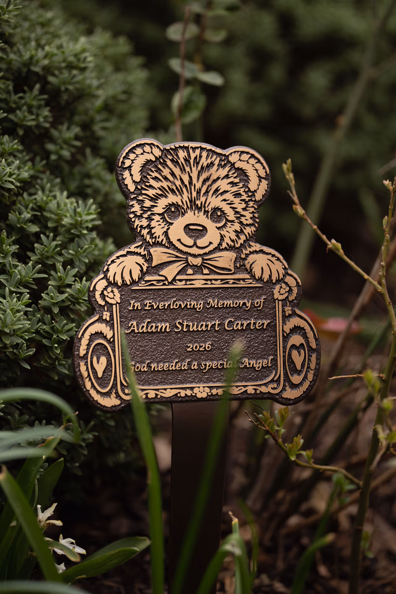 Detailed view of a teddy bear-shaped memorial plaque with raised text, suitable for remembrance gardens.