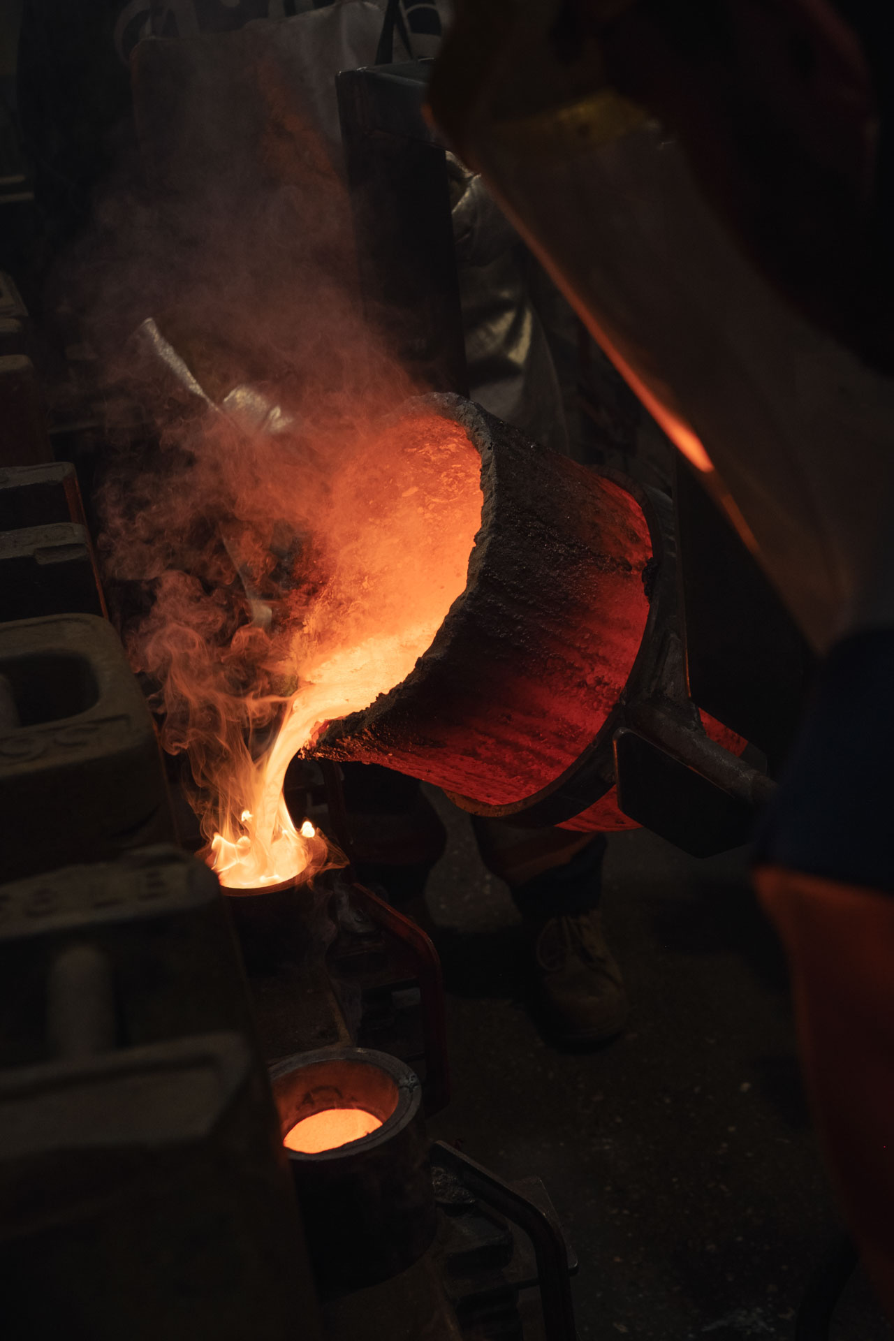 Molten bronze being expertly poured from a glowing crucible into moulds at a traditional foundry, showcasing the craftsmanship behind bespoke cast bronze plaques and memorial signage.