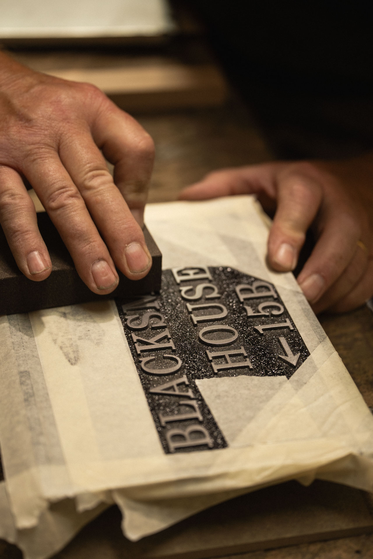 Craftsman hand sanding raised lettering on a bespoke aluminium house sign in the Anglia Sign Casting workshop.