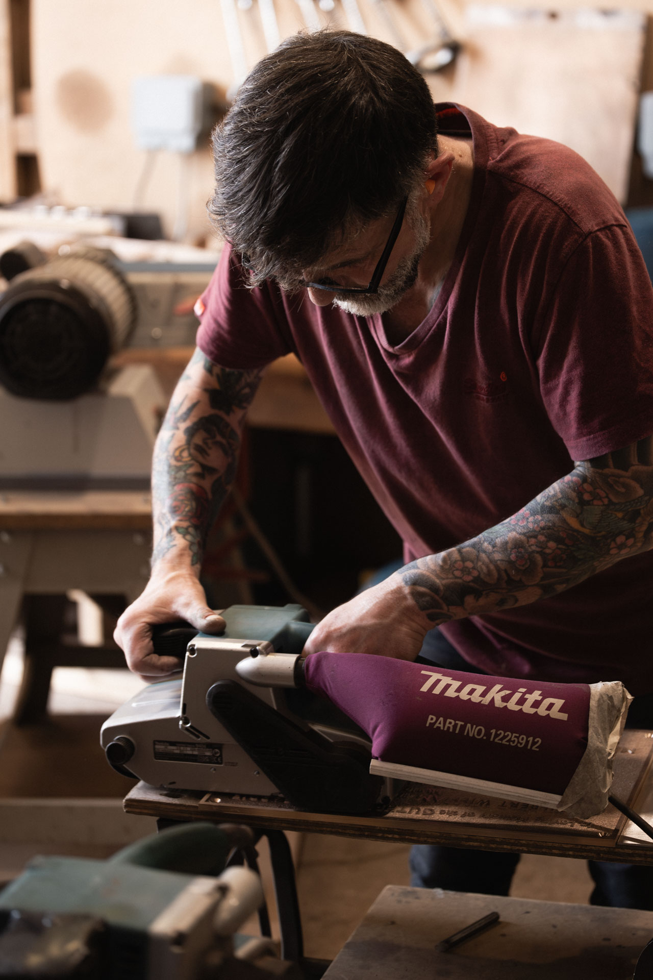 A craftsman using a belt sander to hand finish a bespoke cast metal plaque in the Anglia Sign Casting workshop.