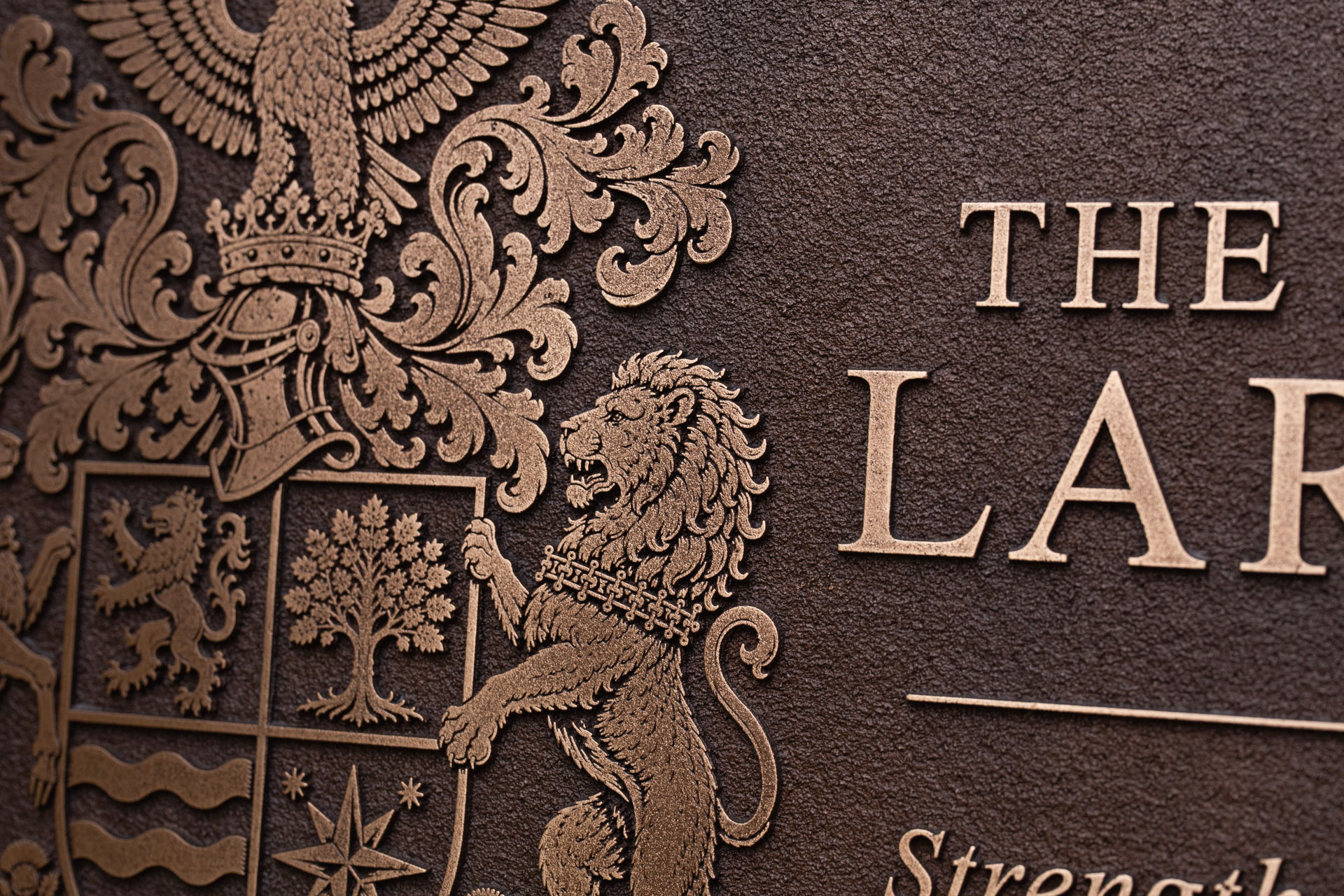 Close-up of an ornate cast bronze family crest plaque showing detailed relief work and polished bronze finish.