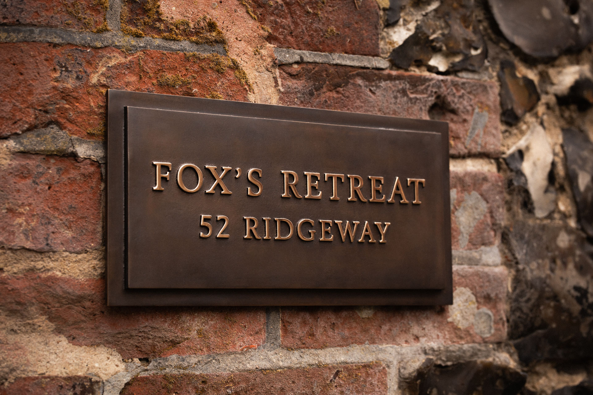 Traditional cast bronze house name sign with polished bronze letters, dark patina finish and raised border.