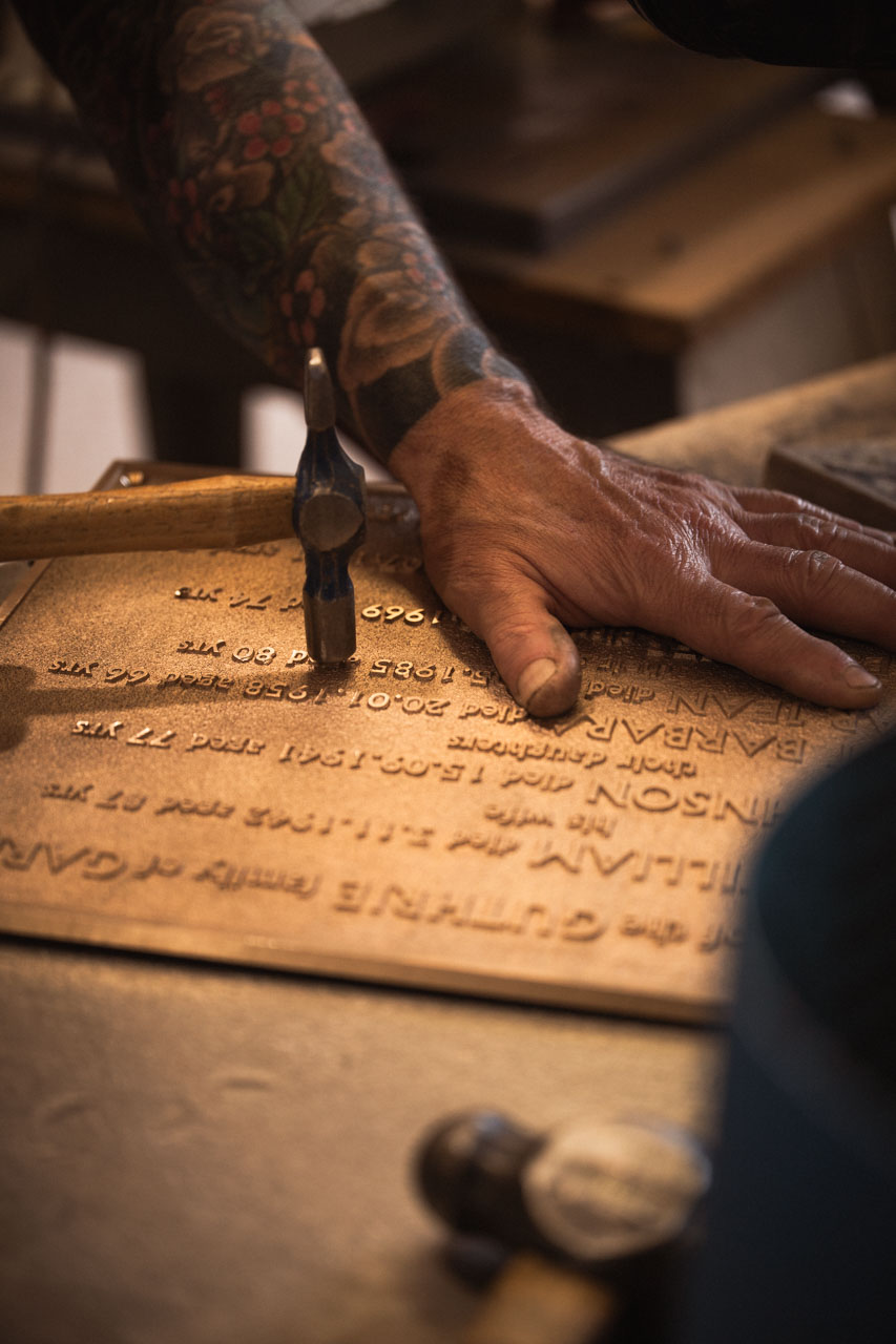 Craftsman hand-finishing a cast bronze plaque with traditional tools during the fettling stage of production.