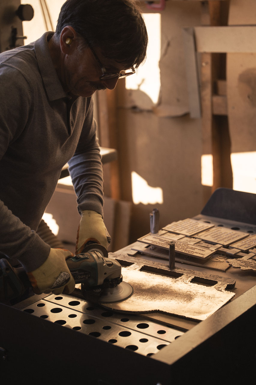 Craftsman grinding and smoothing the back of a cast bronze plaque during the hand-finishing process.