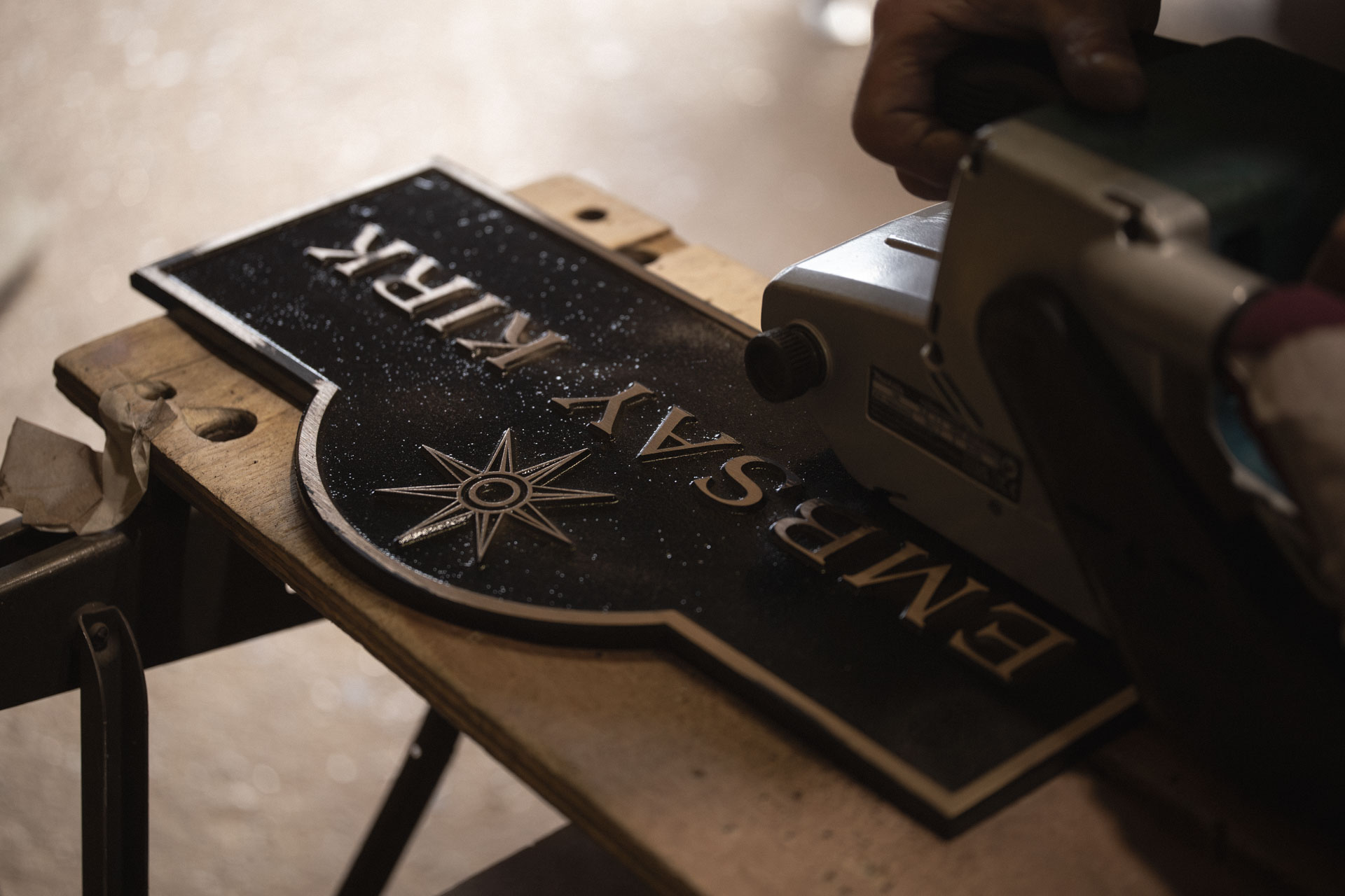 Craftsman carefully sanding the raised bronze lettering on a handmade cast house sign during the finishing process.