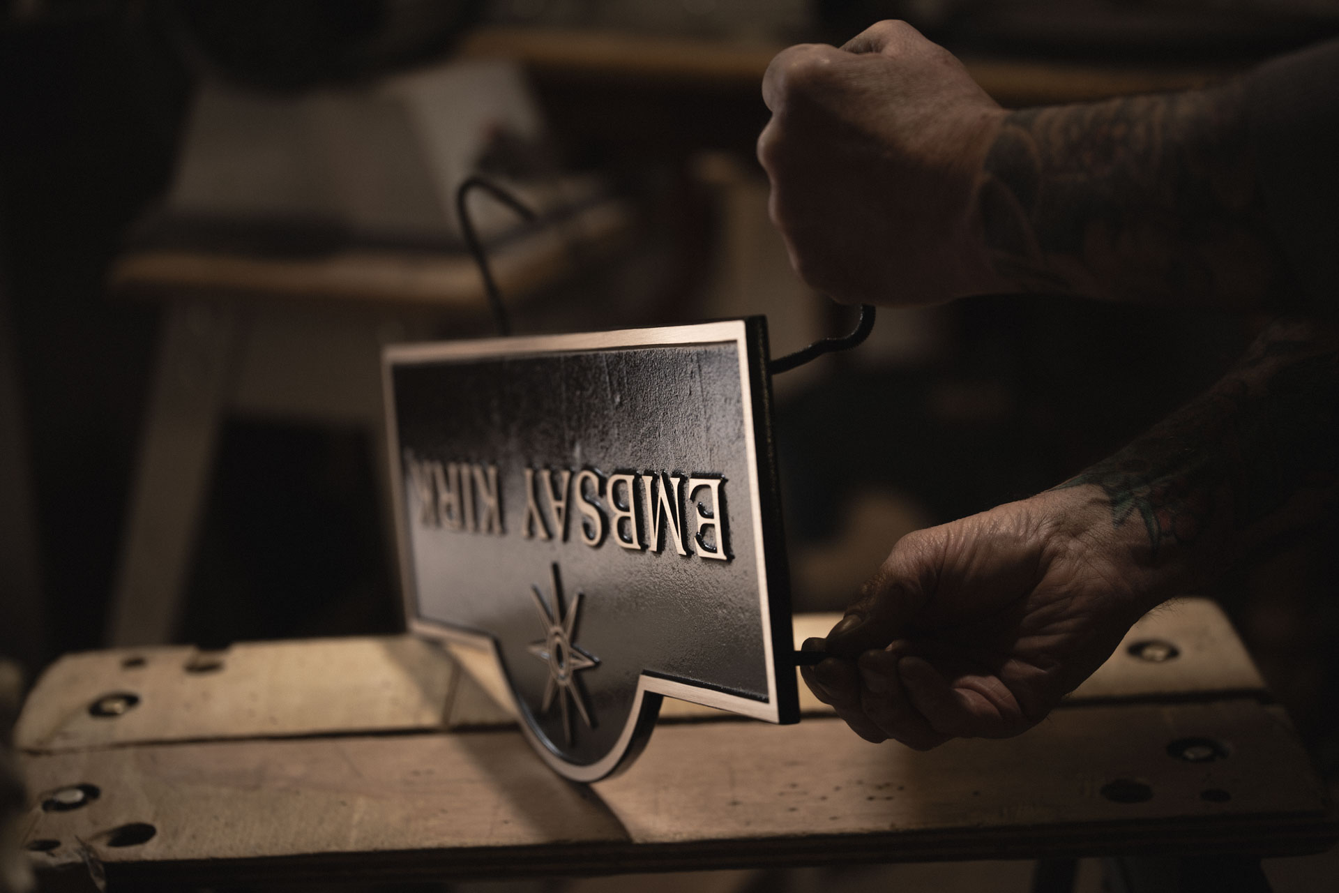 Craftsman fitting the rear fixings by hand to a cast bronze house sign as part of the final finishing and assembly process.