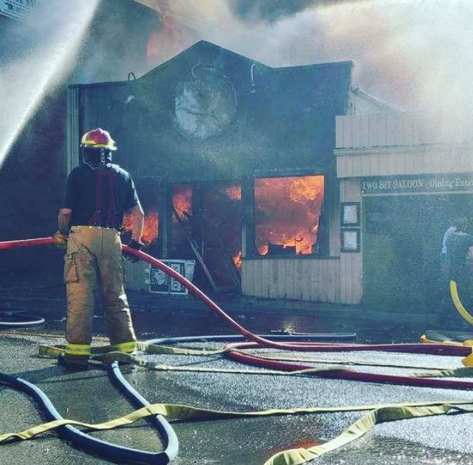 The Two Bit on fire in 2020 in Gardiner Montana, with a fire fighter hosing the flamesi