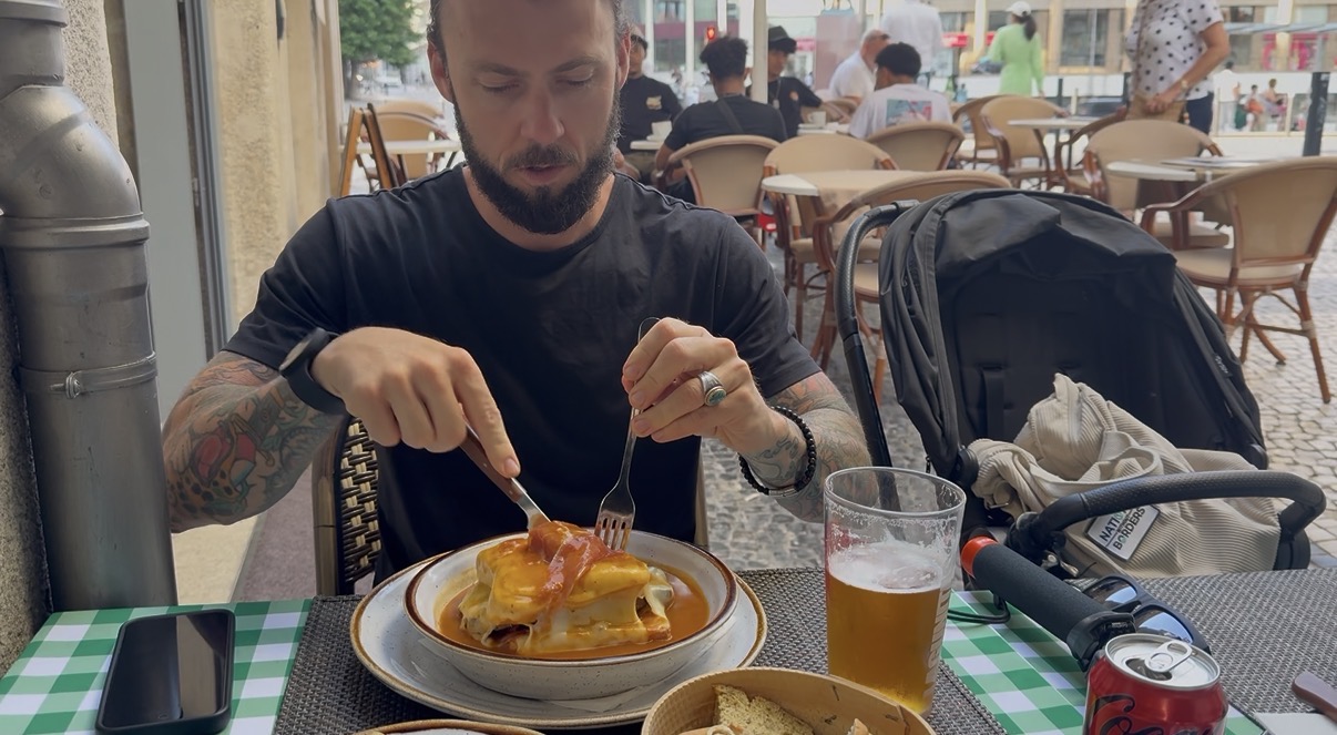 Eric eating a francesinha in Porto, Portugal — with the NWB stroller in the background