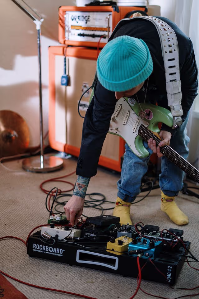 A person holding a guitar while attempting to plug a wire into socket.