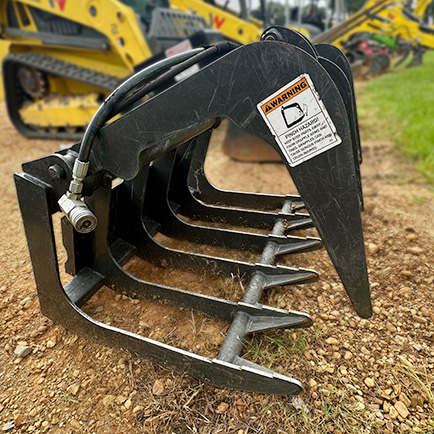 Close-up of black heavy-duty grapple attachment for construction equipment on gravel ground.