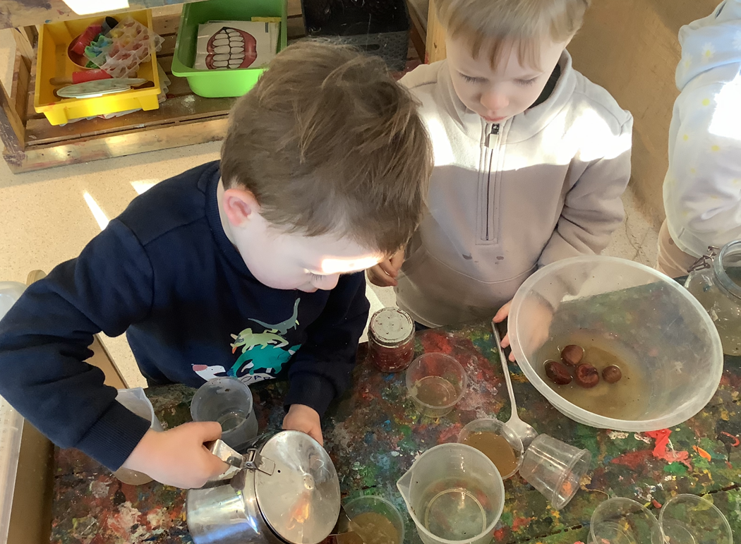 Two children engaging in a messy play activity with water, containers, and chestnuts on a colorful table.