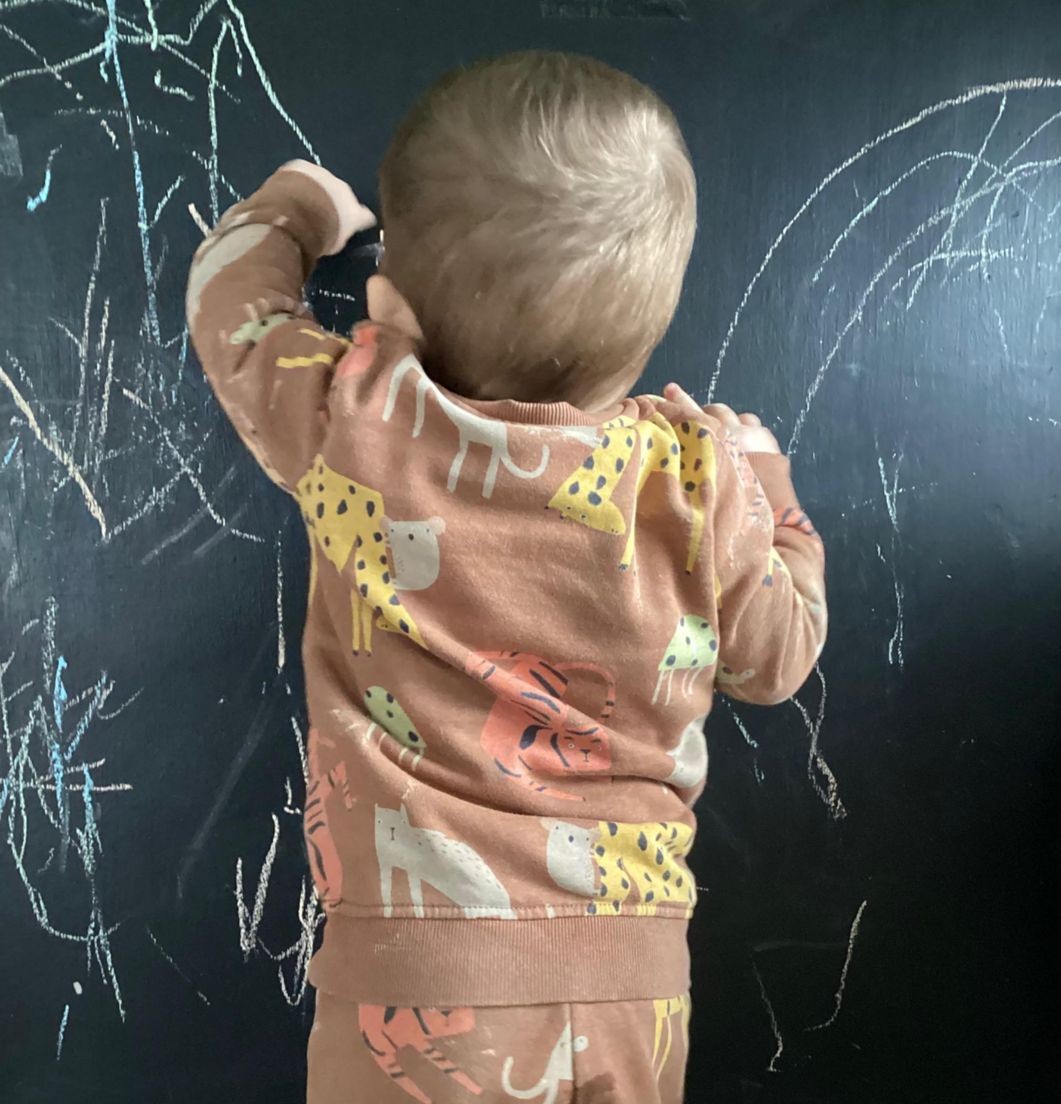 Child wearing animal-patterned pajamas drawing with chalk on a blackboard wall.