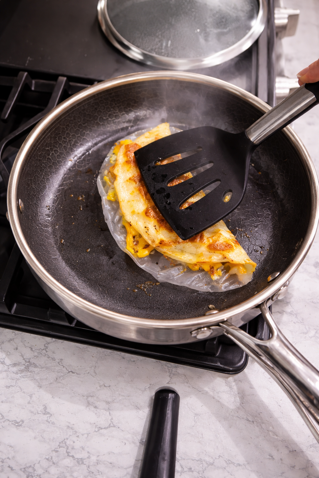 Folding rice paper pizza in a nonstick skillet with a spatula on a marble countertop.