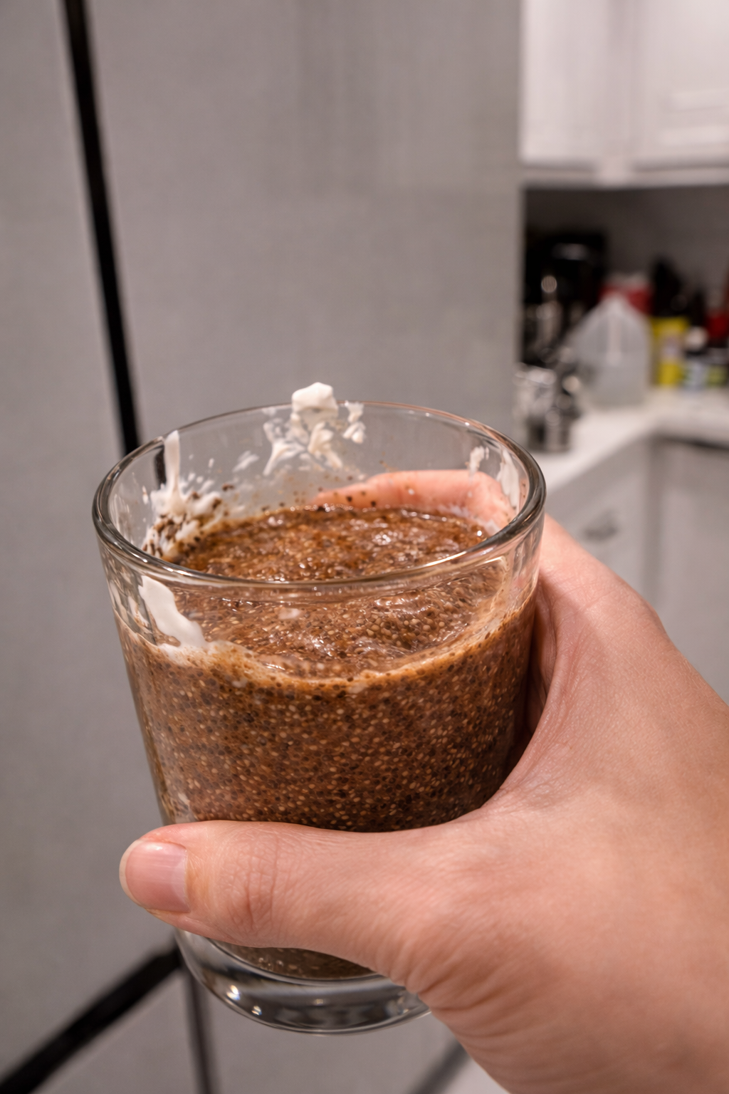 Hand holding a glass of freshly mixed tiramisu chia pudding in a modern kitchen before placing it in the refrigerator to chill.