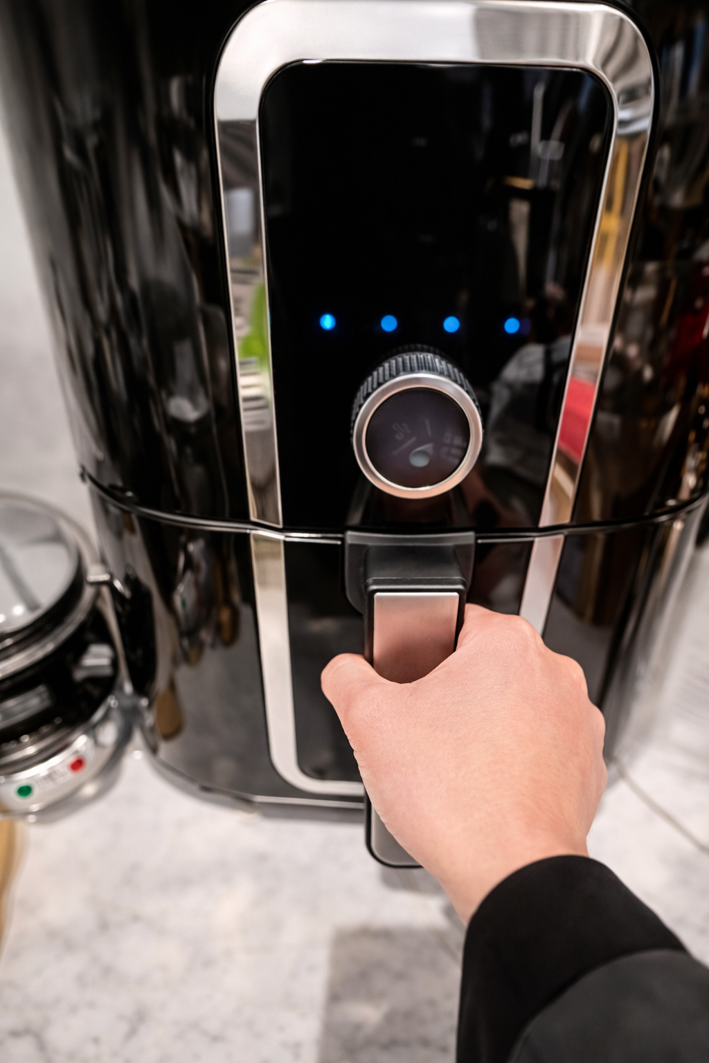 Hand closing a sleek black air fryer drawer on a marble countertop, preparing the seasoned Parmesan pasta to cook into crispy pasta chips.