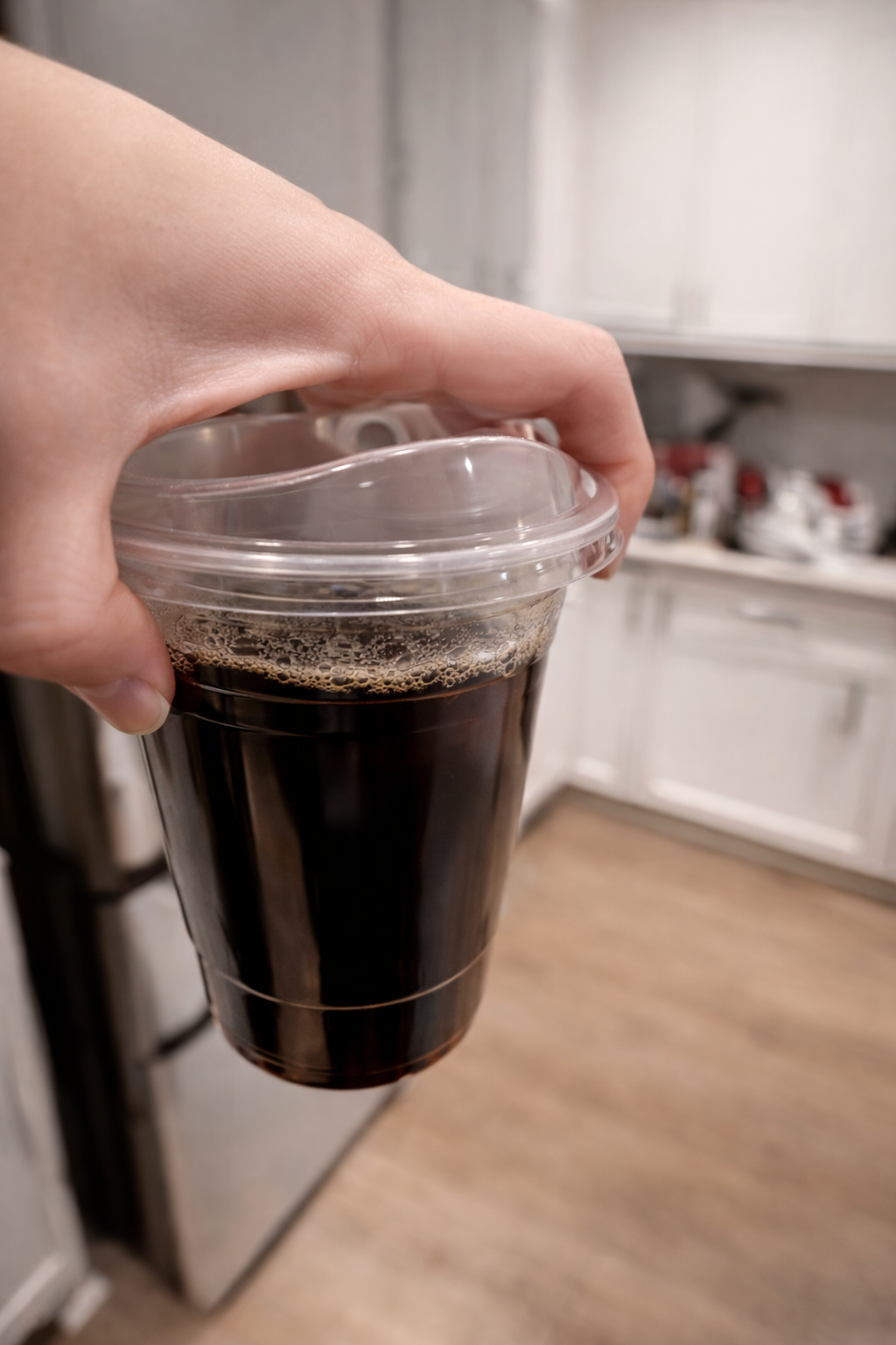Hand holding a cup of freshly brewed coffee jelly mixture in a clear container in a bright modern kitchen with soft lighting.