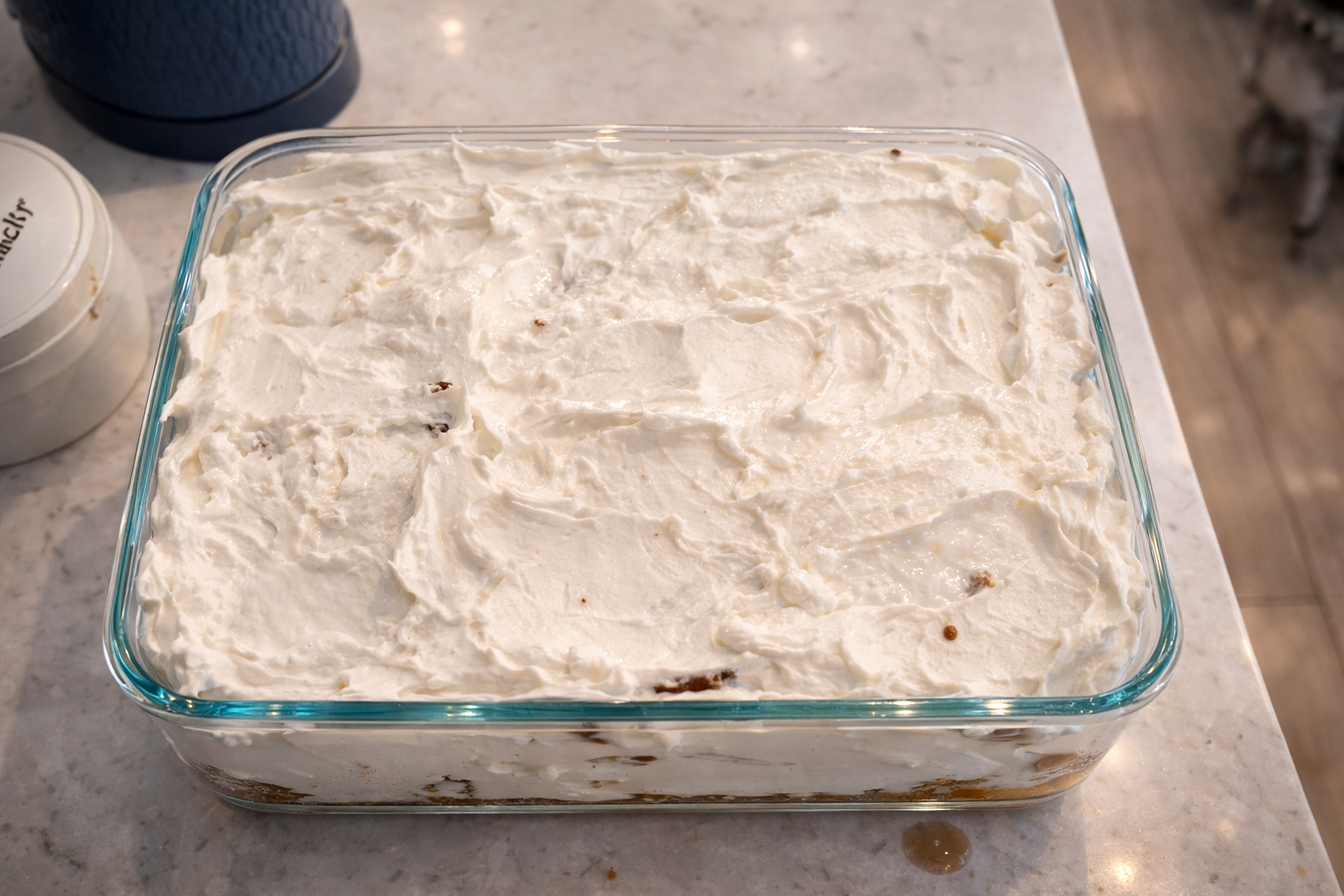 Second layer of creamy cheese and cool whipped mixture spread evenly over tiramisu in a glass baking dish on a kitchen countertop.