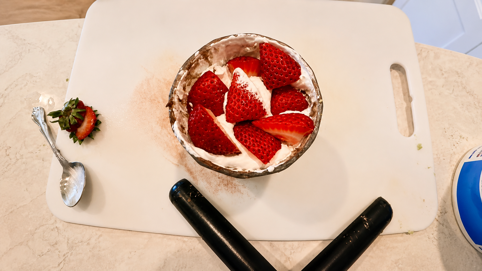 Overhead photo of avocado chocolate mousse topped with whipped cream and fresh strawberries in a glass bowl on a white cutting board in a bright kitchen.