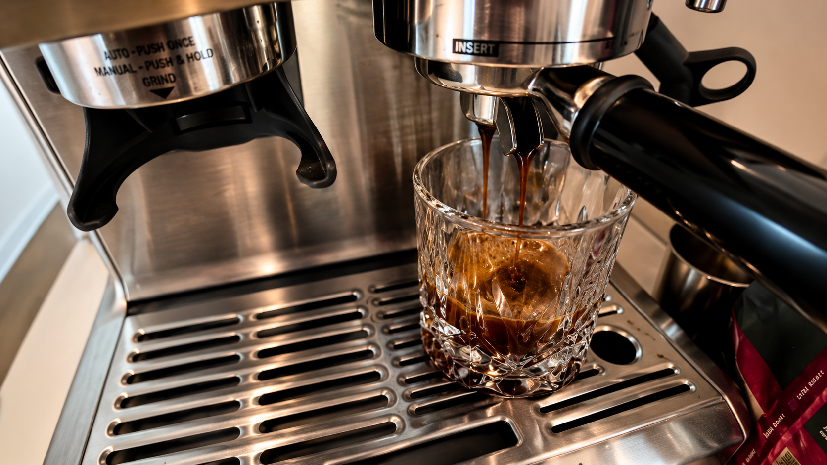 Close-up of a stainless steel espresso machine pouring rich espresso into a crystal glass, photographed with warm lighting and a professional coffeehouse-style food photography aesthetic.