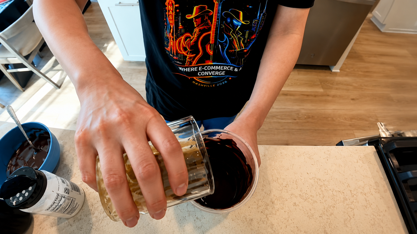 Overhead view of a person pouring a creamy liquid into a chocolate-coated cup in a bright modern kitchen, featuring smooth youthful hands and a professional food photography aesthetic.