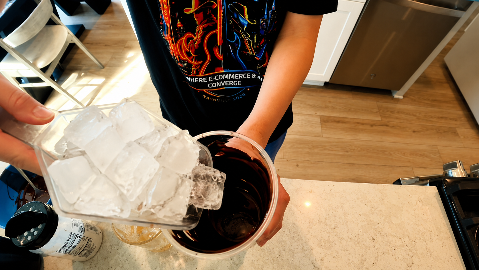 Overhead view of a person pouring crystal-clear ice cubes into a chocolate-coated cup in a bright modern kitchen, photographed with warm natural lighting and a professional food photography aesthetic.