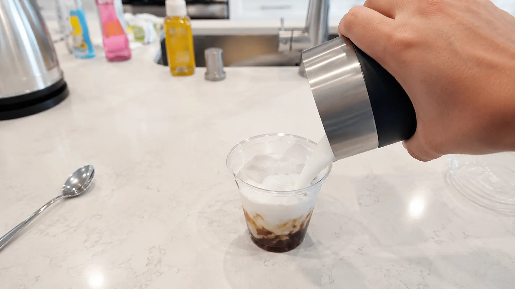 pouring frothed milk onto iced espresso