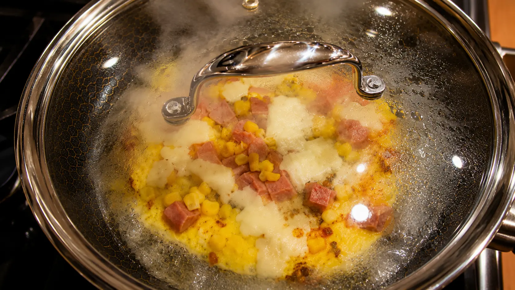 Rice paper pizza with egg, mozzarella, hot dogs, and corn cooking under a glass lid in a nonstick skillet.