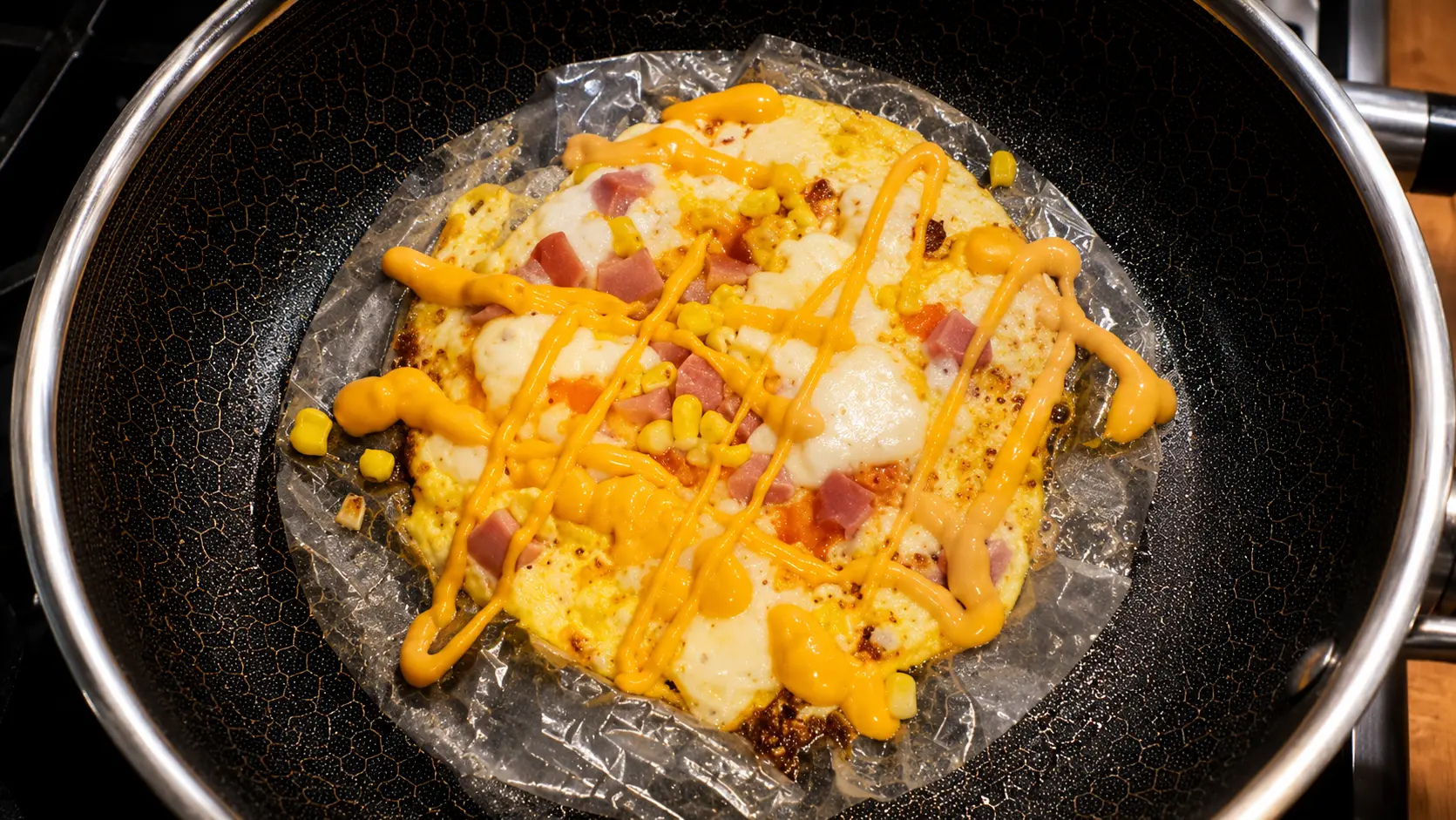 Rice paper pizza topped with melted mozzarella, diced hot dogs, corn, and sriracha mayo in a nonstick skillet.