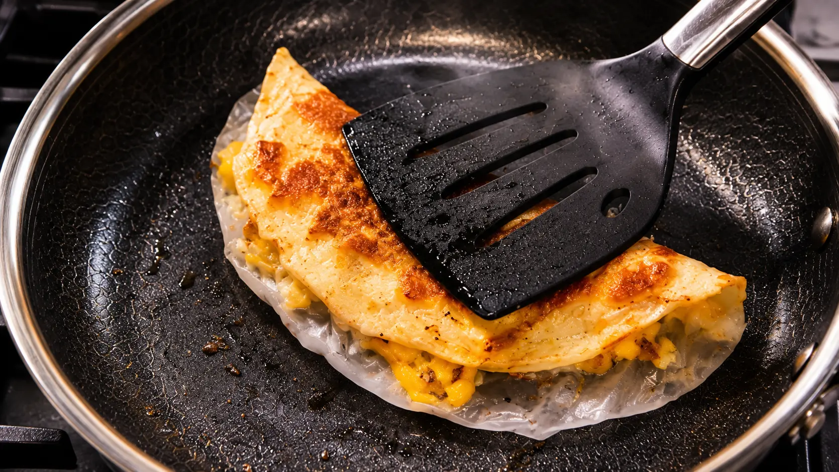 Folding rice paper pizza in a nonstick skillet with a spatula on a marble countertop.