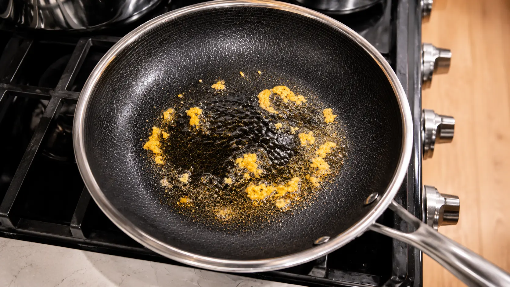 Close-up of minced garlic sizzling in olive oil inside a nonstick skillet on a stovetop, the golden pieces gently browning and glistening under warm kitchen lighting.