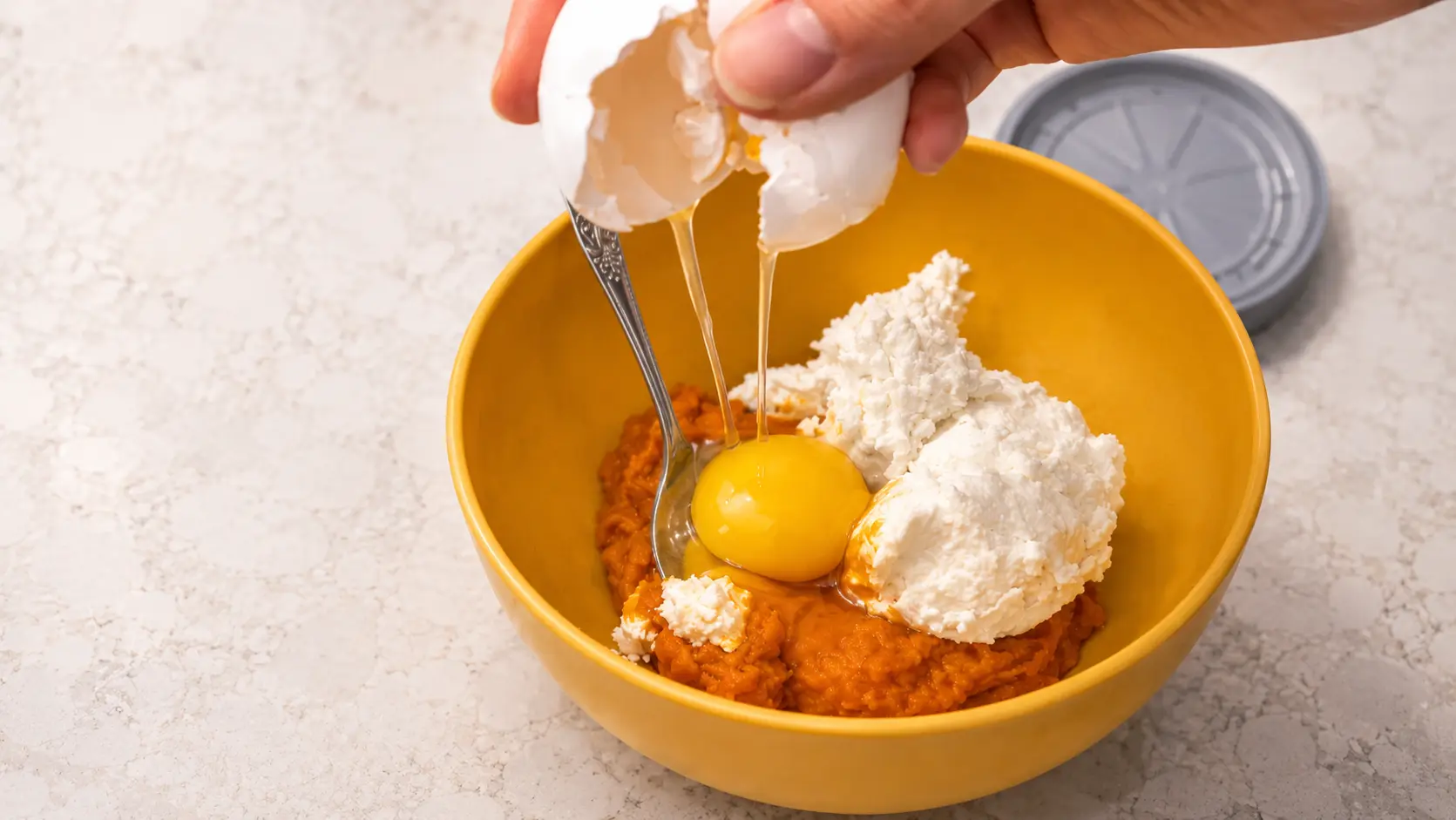 cracked an egg in a pumpkin puree with cream cheese mixture in a yellow bowl