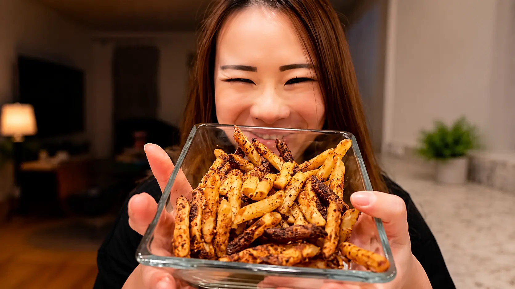 **Alt Text:**  *A smiling woman holds a glass bowl filled with crispy, golden-brown pasta chips seasoned with herbs, Parmesan cheese, and spices. The bowl is presented toward the camera, showcasing the crunchy texture and toasted edges of the pasta chips. Warm, professional food-photography lighting highlights the snack while the cozy kitchen background fades into a soft blur, creating an inviting, restaurant-quality presentation. The woman’s cheerful expression adds a sense of excitement and satisfaction as she shares the finished dish.*