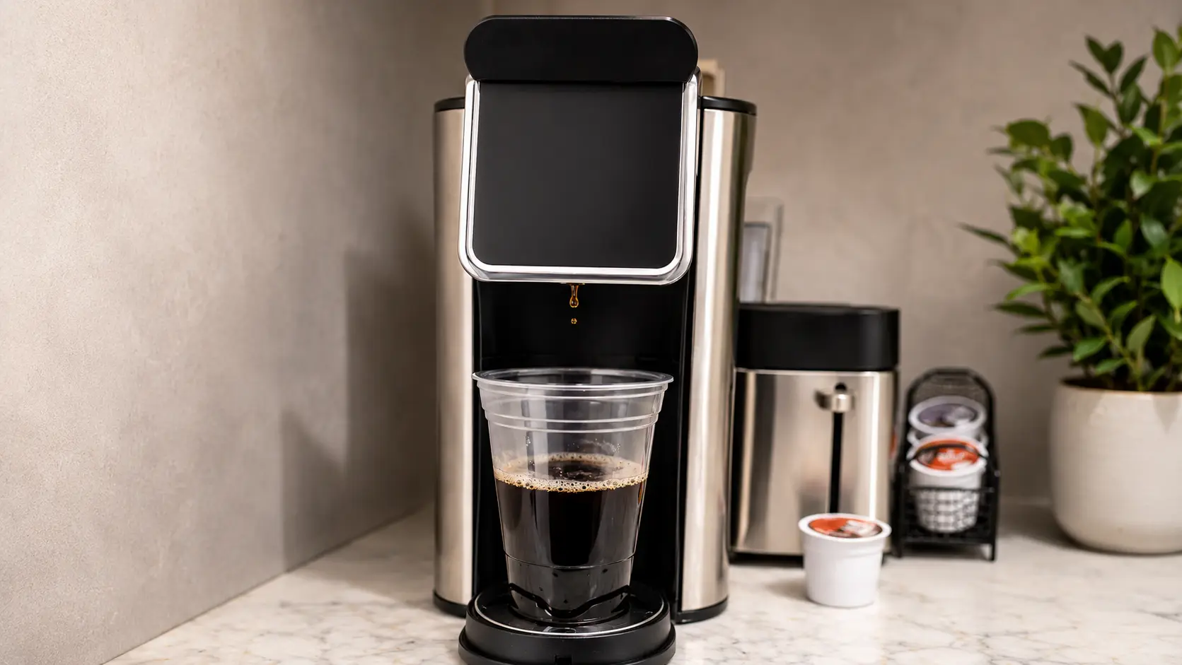 **Alt Text:** *A professional food-photography image of freshly brewed black coffee dispensing from a sleek stainless-steel coffee maker into a clear plastic cup. A single droplet of coffee is captured mid-fall beneath the dispenser, adding a sense of motion and freshness. The rich, dark coffee contrasts beautifully with the light marble countertop, while soft natural lighting and a shallow depth of field create a clean, modern café-style aesthetic. The background is softly blurred, drawing attention to the brewing process and the deep color of the coffee.*