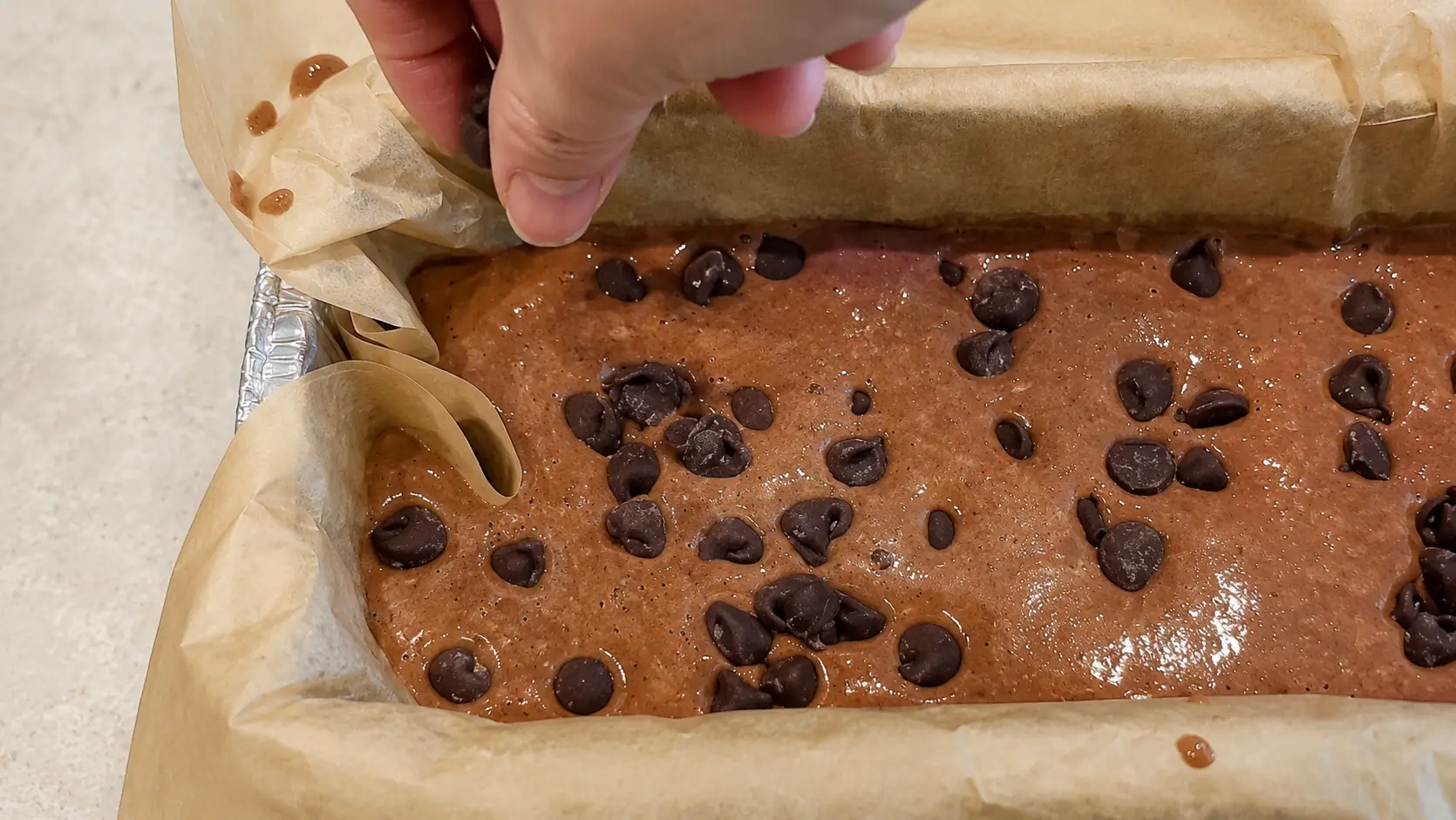 Chocolate chips topping flourless high protein brownie batter made with banana, eggs, Greek yogurt, honey, and cocoa powder before baking.