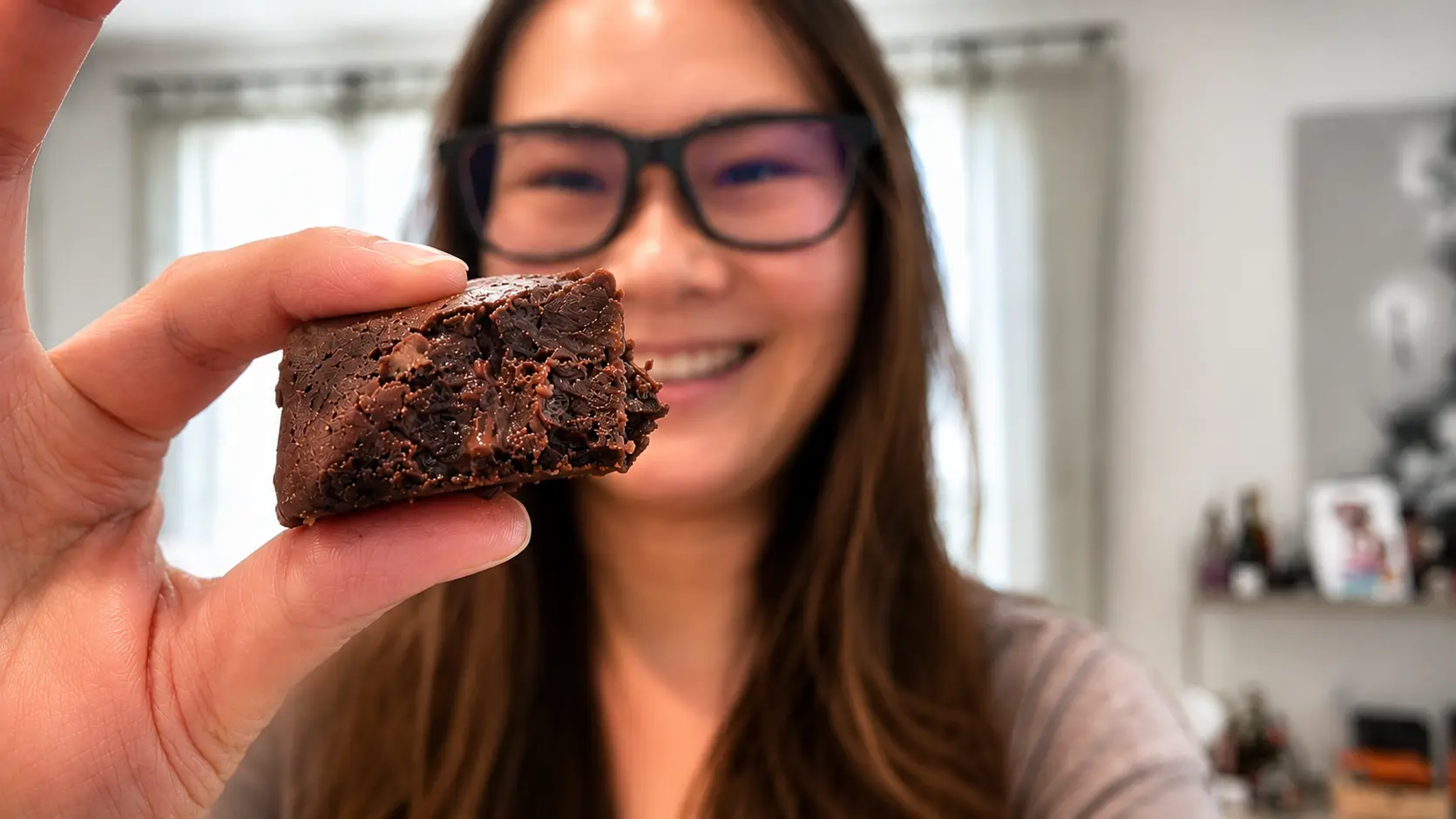 Fudgy high protein brownie held in front of the camera with a soft background blur. The flourless brownie features a rich chocolate texture and decadent chocolate chips.